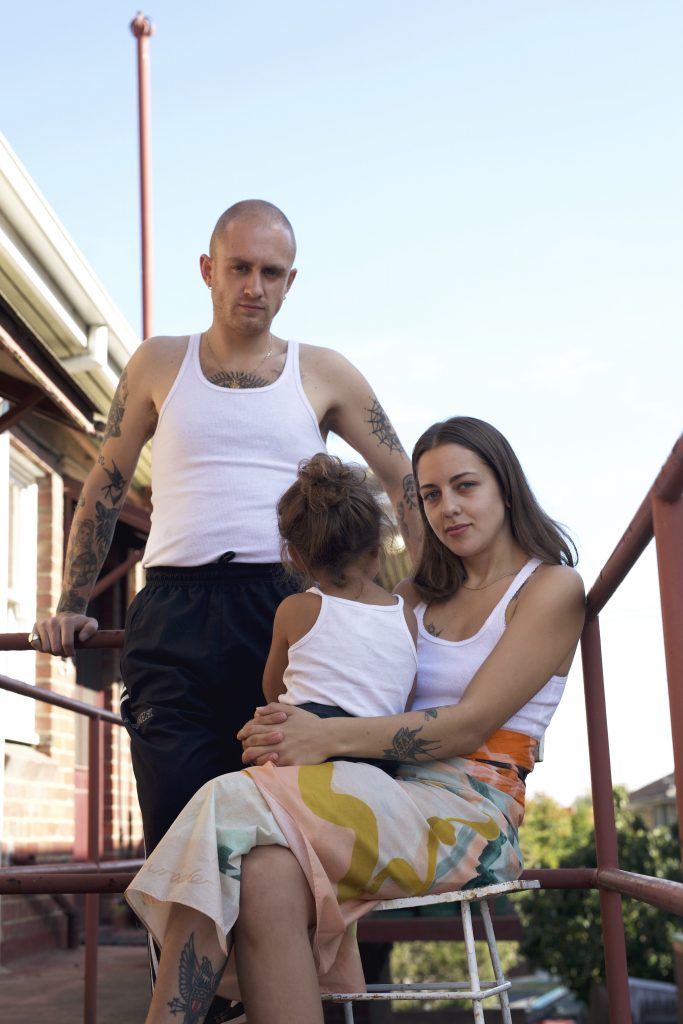 The author sits with her child and her child's other parent stand behind them. They are all wearing white singlets.