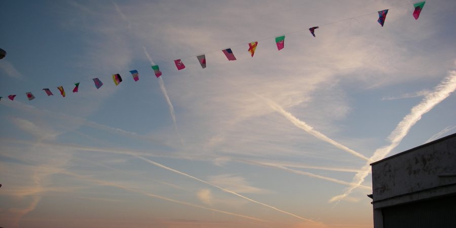 A series of flags against a cloudy sky, representing international travel.