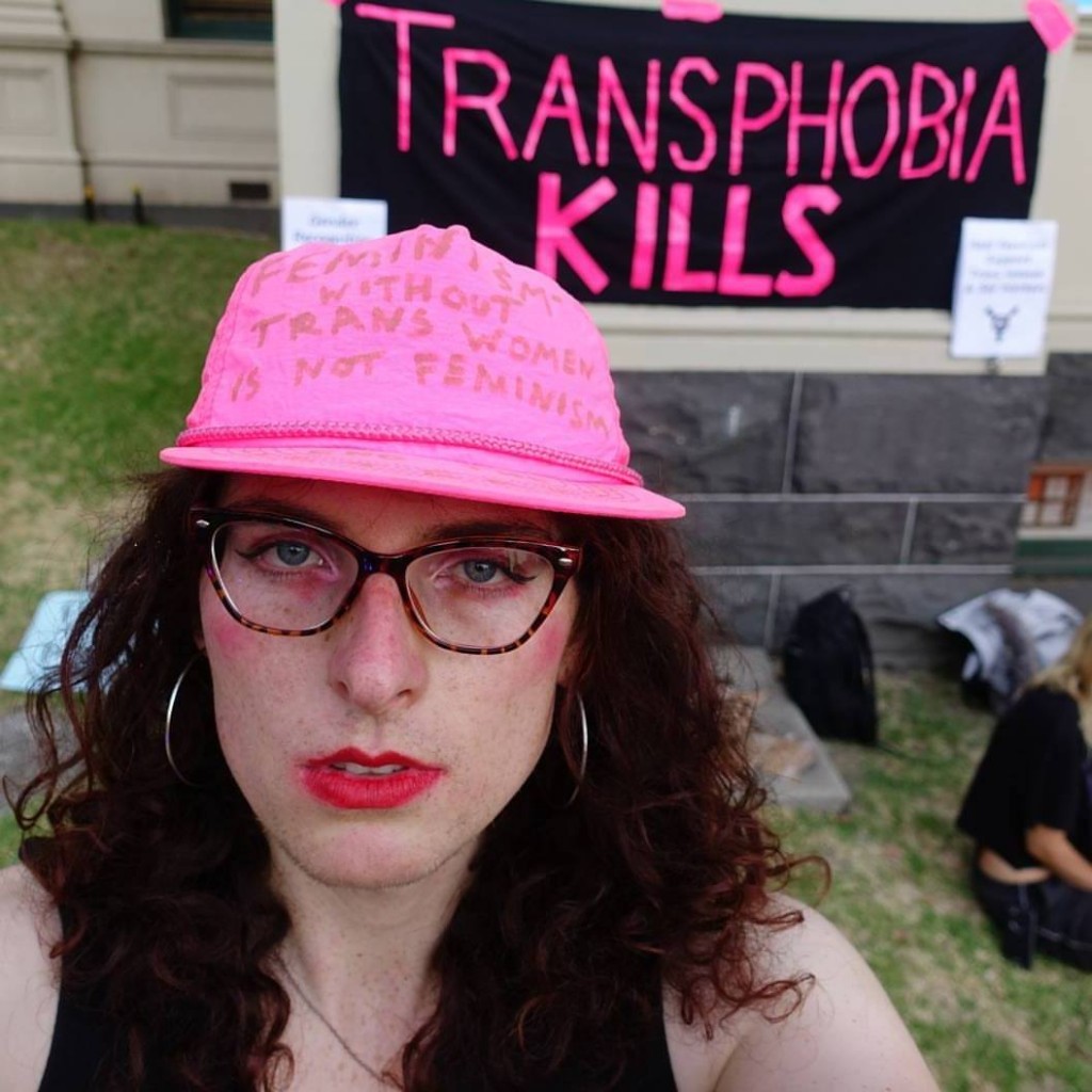 the writer in front of 'transphobia kills' banner to TERFs