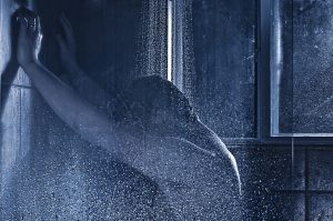 A male figure presses their hands onto the wall of the shower