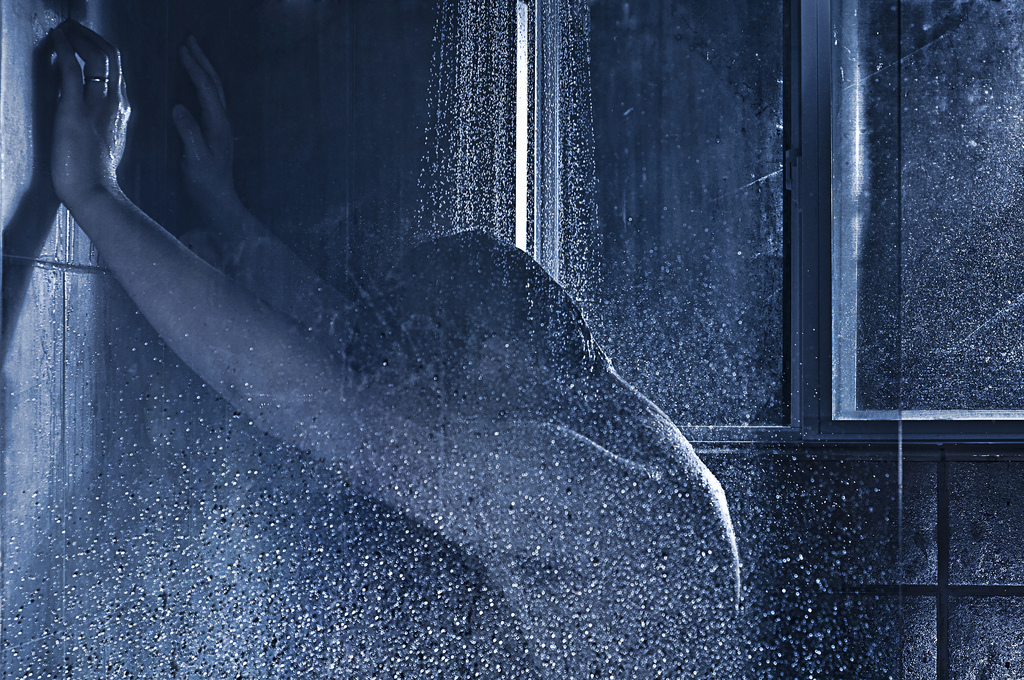 A male figure presses their hands onto the wall of the shower prep