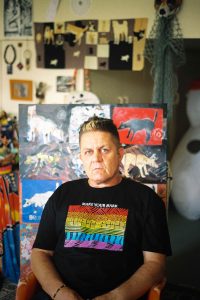 Peter Waples-Crowe facing the camera wearing a black tshirt with a rainbow Indigenous artwork on the chest and the words 'make your mark'