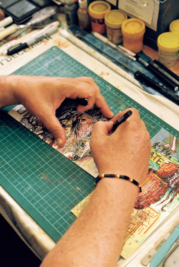 Peter's hands are seen from above as they sketch a line drawing. Peter is wearing a beaded bracelet in Indigenous flag colours.