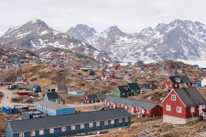 The town of Tasiilaq, Greenland, is in the foreground, with a mountainous landscape in the background. The town is dotted with colourful buildings.