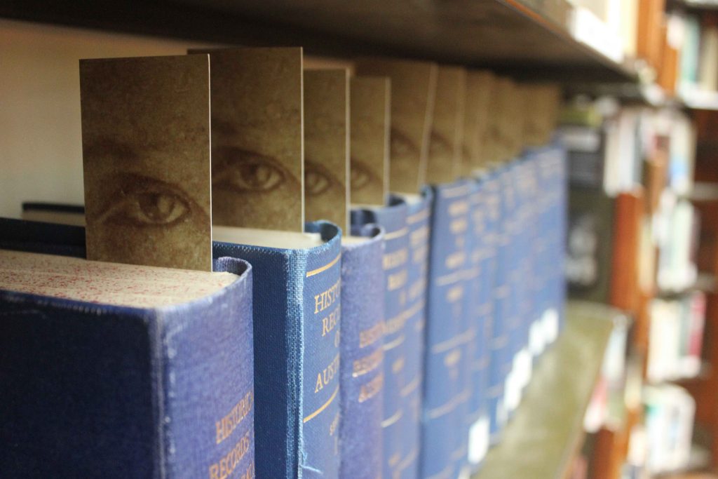 A row of blue books each have a bookmark with an eye on it sticking out the top of the book. 
