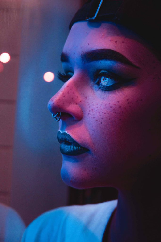 Photo of person with black lipstick and nose piercings captured inside dim light room