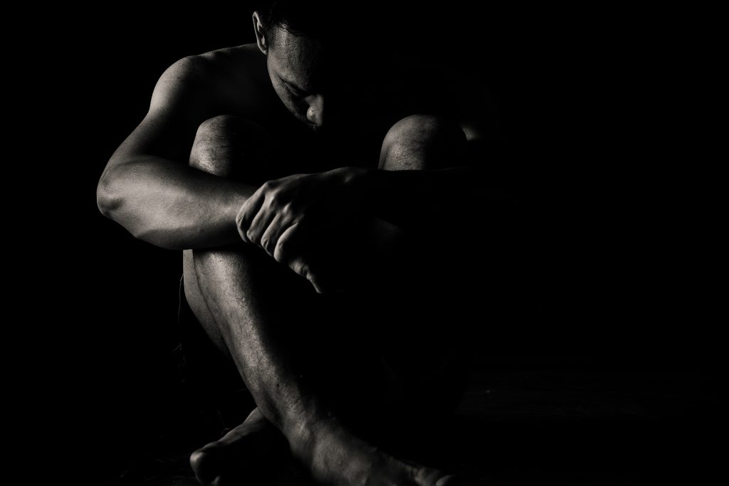 a person sits with their legs crossed and head in their knees in the shadows