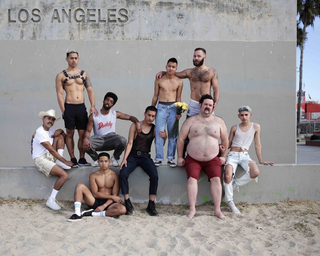 a group of 9 people of different races and sizes are grouped in front of a sign that reads 'Los Angeles'