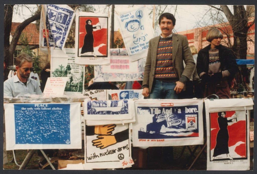 McGahen stands at a stall selling tea towels with left wing slogans on them.