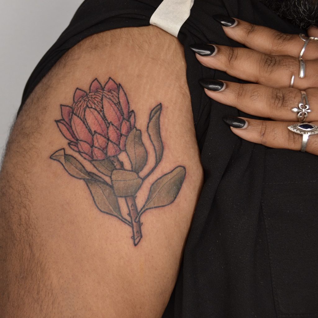 A tattoo of a waratah on a person's arm. You can see their hand, with long, painted fingernails holding their shirt back.
