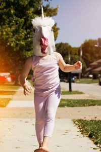a person wearing a unicorn costume head walks down the street