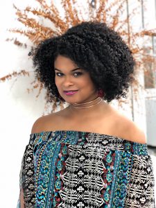 Raquel Willis faces the camera, standing in front of a plant.