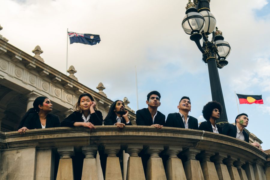 A group looks out off a balcony, with the Australian flag and Aboriginal flag behind them