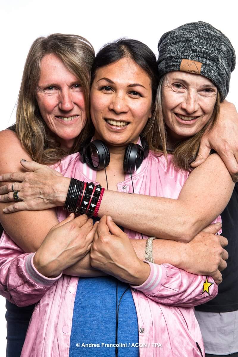 Three smiling women embrace side by side