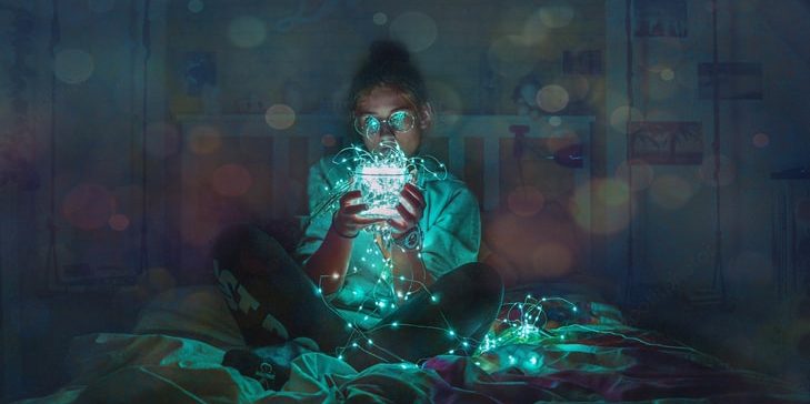 Image: Person sitting on bed holding box of glowing fairy lights