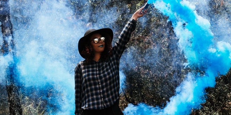 Person wearing hat and sunglasses holding flare with blue smoke