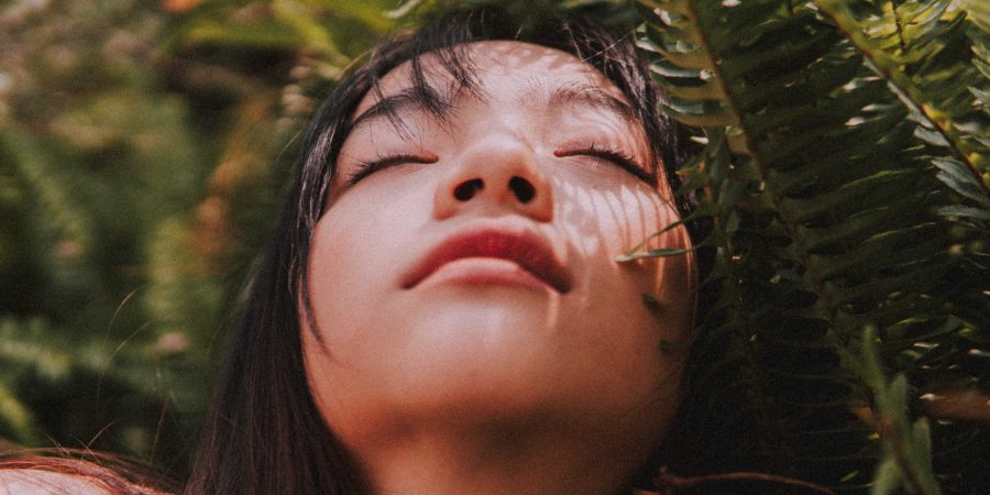 Close up of persons upturned face with eyes closed in apparent pleasure, surrounded by ferns