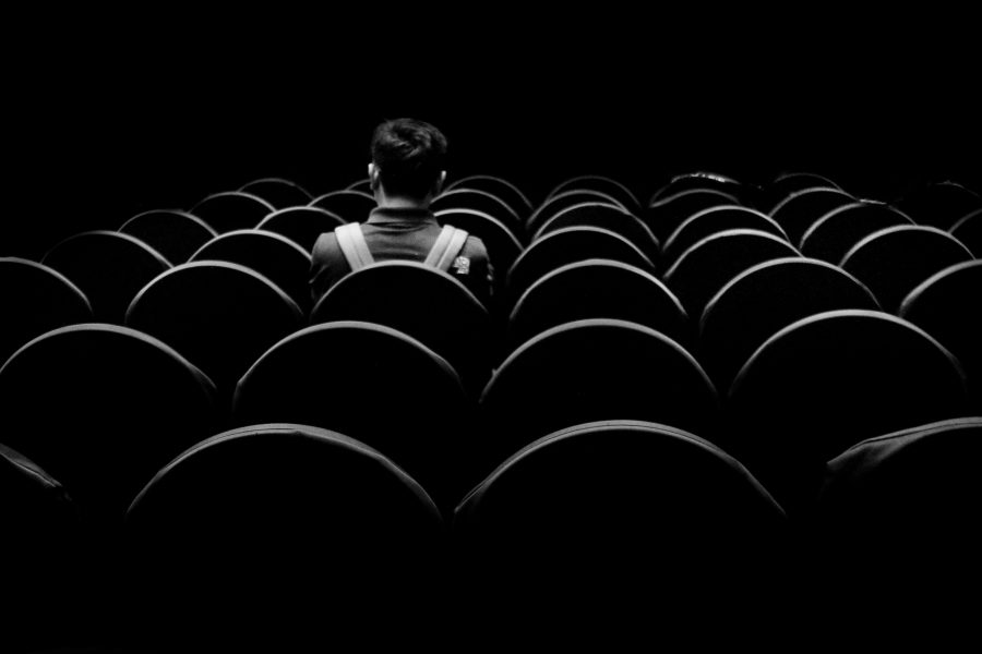 Person wearing a jacket and backpack sitting in an empty cinema