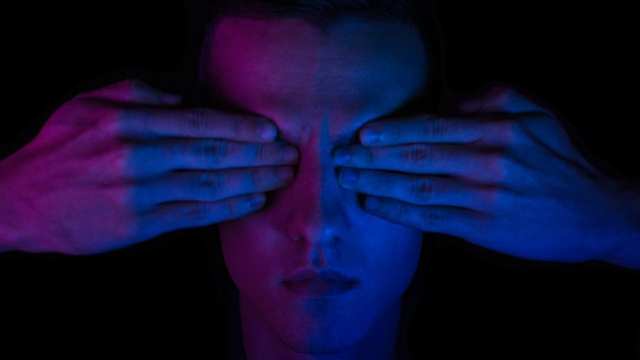 A person with hands over their eyes, bathed in pink and blue light