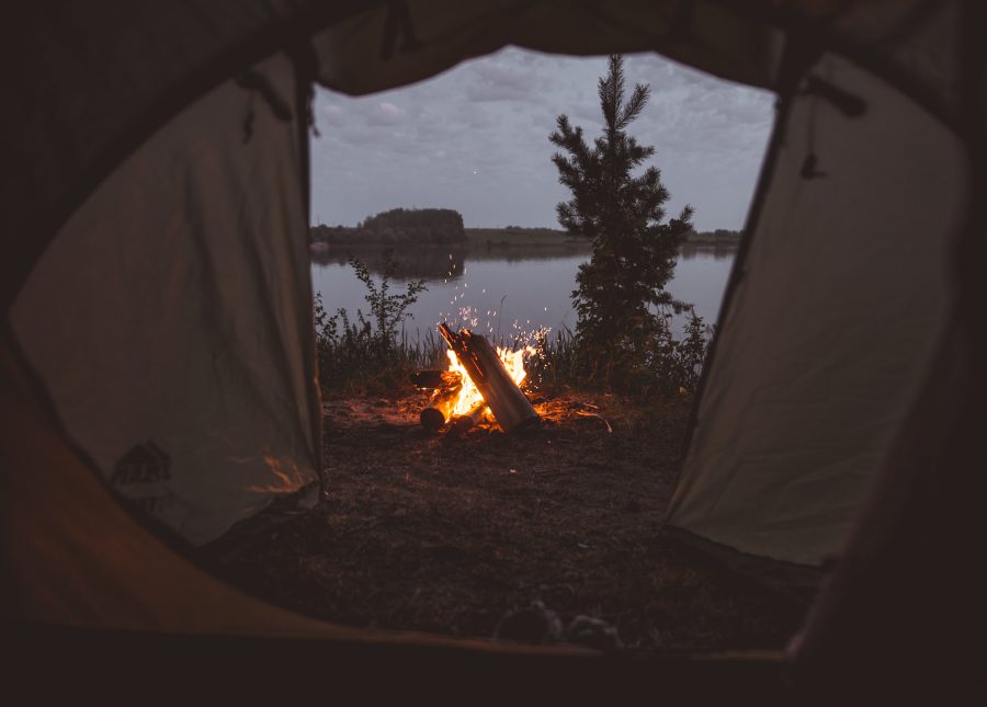 A small campfire at dusk, captured through the open entrance of a fabric tent.