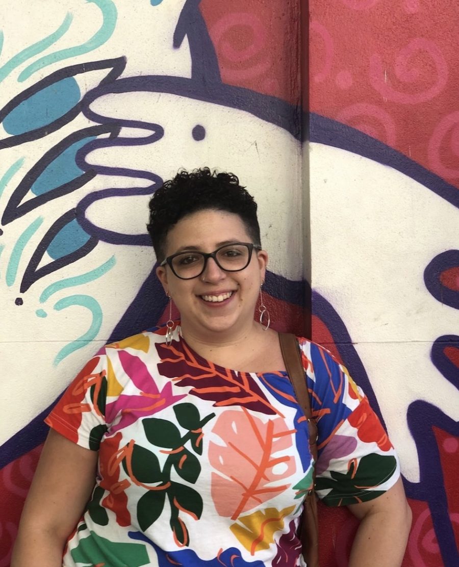 Image of Roz wearing a colourful patterned shirt in front of red, white, blue and black street art