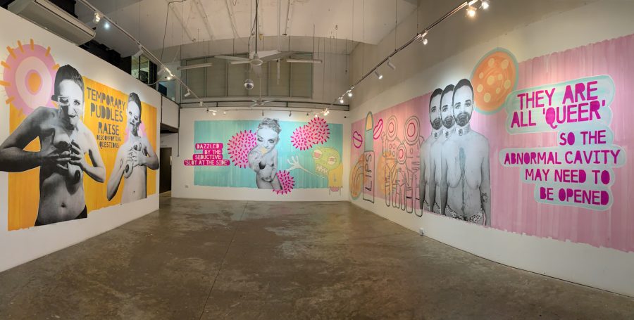 A photo of a large art gallery. The image shows three different artworks that are brightly coloured and pop-art style, with varying words about queer expression.
