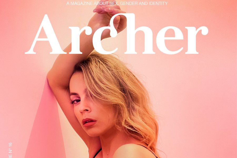 A femme person with blonde long hair is seen resting their arm up against a pink wall. In white text above their long blonde hair, it says 'Archer', indicating that this is a cover photo for the upcoming Archer issue.
