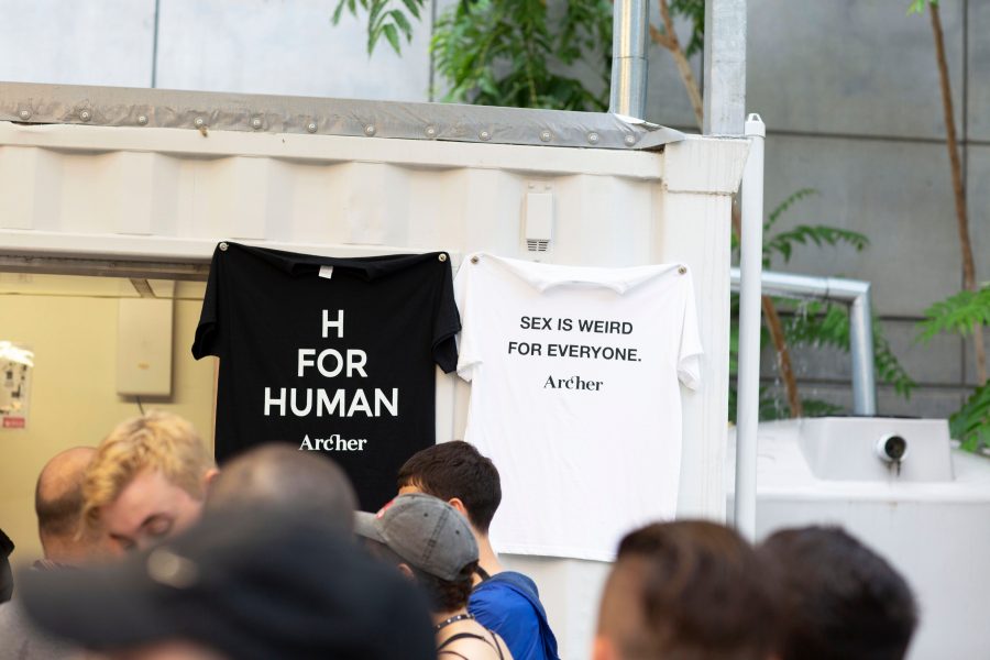 In this photo, you can see the corner of a shipping container that has been turned into a bar. Hanging up near the window on the shipping container are two shirts. One is black and says "H FOR HUMAN", and one is white and says "SEX IS WEIRD FOR EVERYONE".