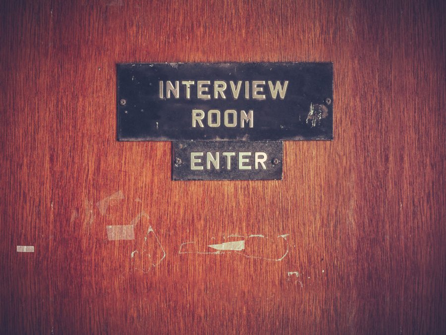 A grungy wooden door with a sign that reads "INTERVIEW ROOM" and another beneath it that reads "ENTER".