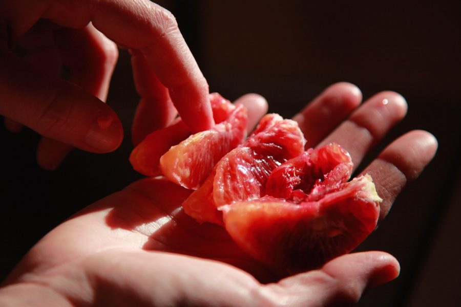Glistening segments of blood orange are held in the palm of one hand, touched lightly by the fingers of another.