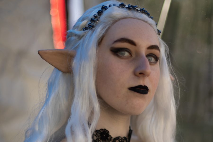A person with a white long wig and elf ears stares into the camera. They are a LARP character; they have dark lipstick and a flower crown.