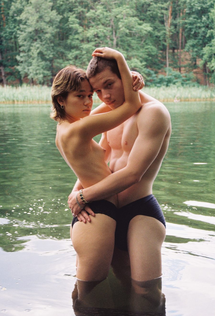 Two people embracing in knee-deep water. They are looking at the camera.