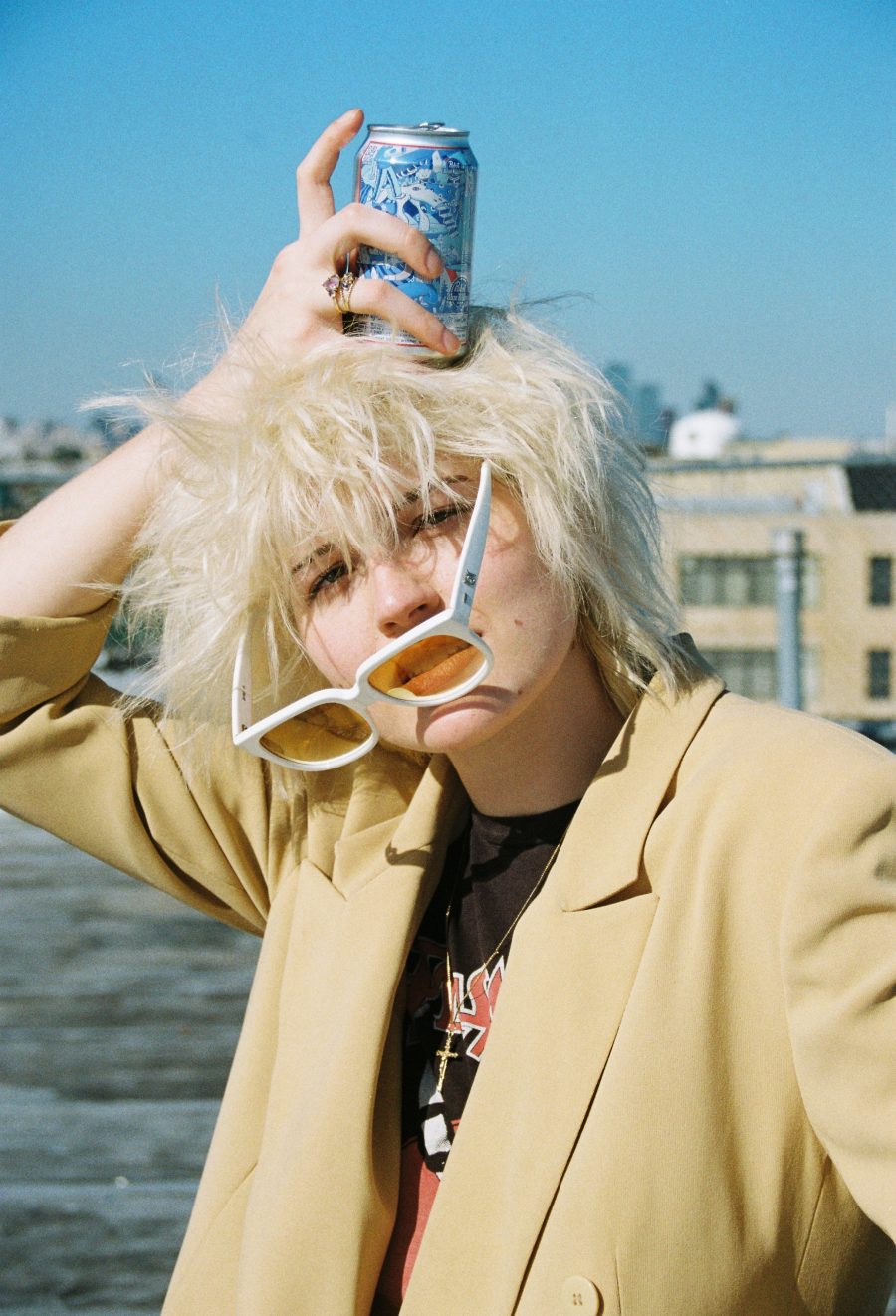 A person holding a can of soda to the top of their head as glasses slide down their face.