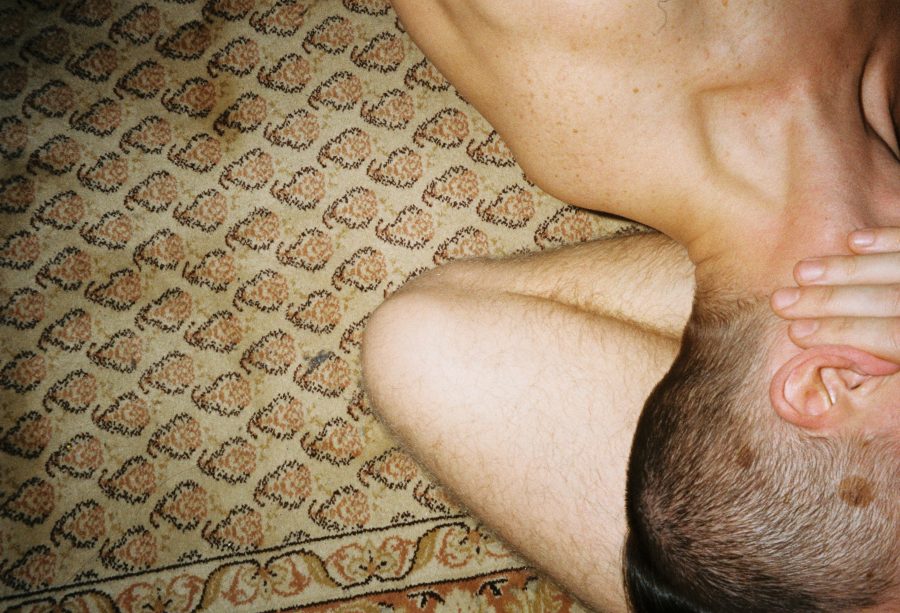 The side of one person's head as they are embraced by another person's arm on patterned carpet.