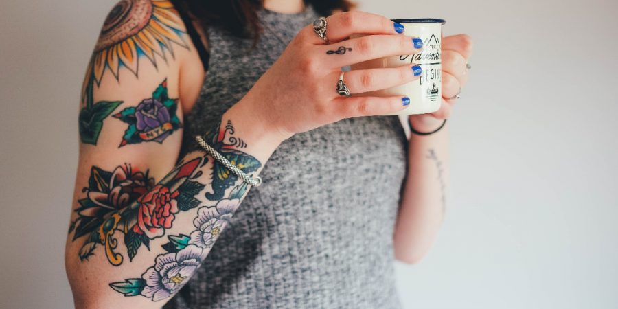 A tattooed person holding a mug.