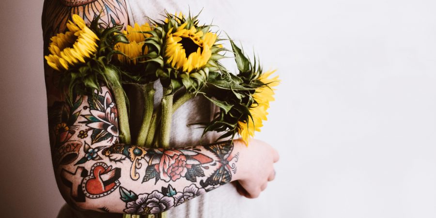 A tattooed person holding sunflowers.
