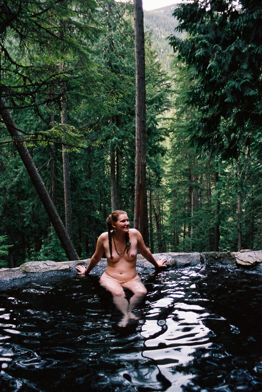 A person sitting on the edge of a hot spring and smiling.