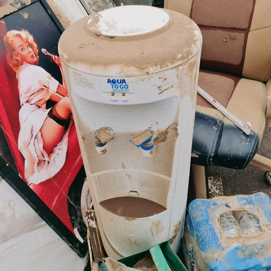 A water cooler covered in mud, next to a poster with a model on it.