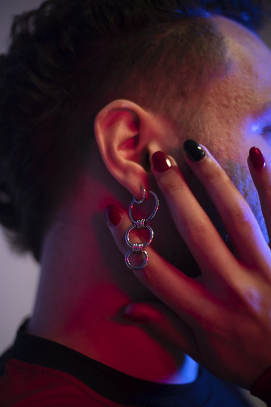 An image of Ulysses' earring and their hand with nail polish on their fingernails.