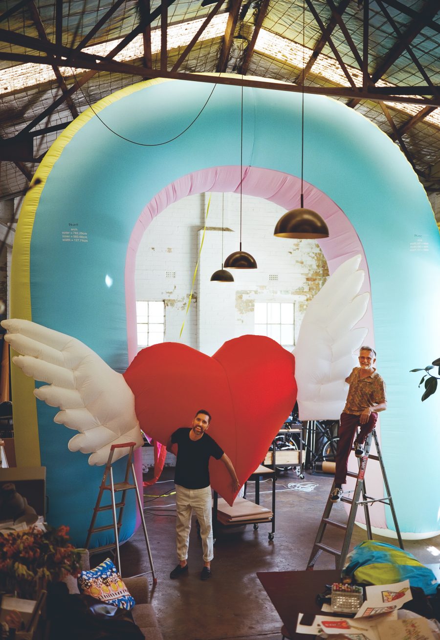 Two people in an art studio in front of a huge inflatable rainbow and heart. Taken by Liz Ham.