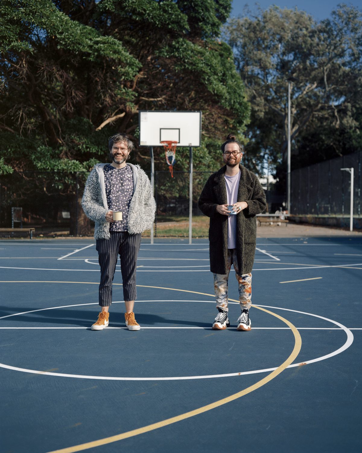 Two people smiling on a basketball court holding mugs of coffee. Taken by Liz Ham.