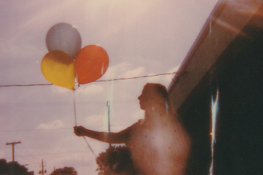 A person's silhouette holding three colourful balloons.