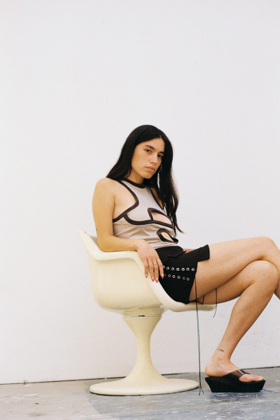 A model sitting in a chair, wearing an outfit by Spitsubishi.
