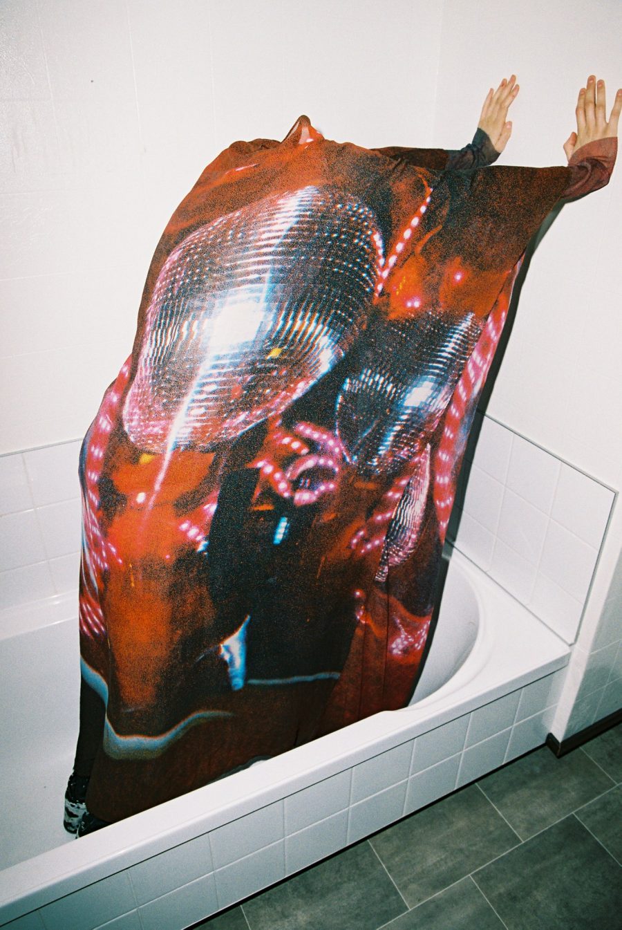 A person in a bathtub, obscured by fabric with a disco ball design on it.