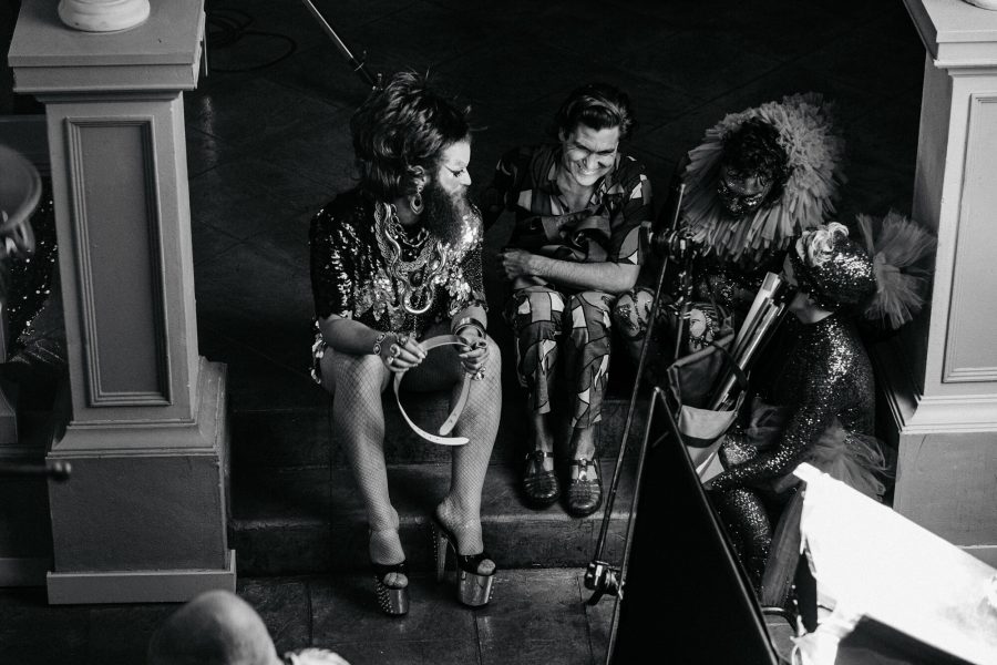 A black-and-white image of queer performers sitting on some stairs and chatting.