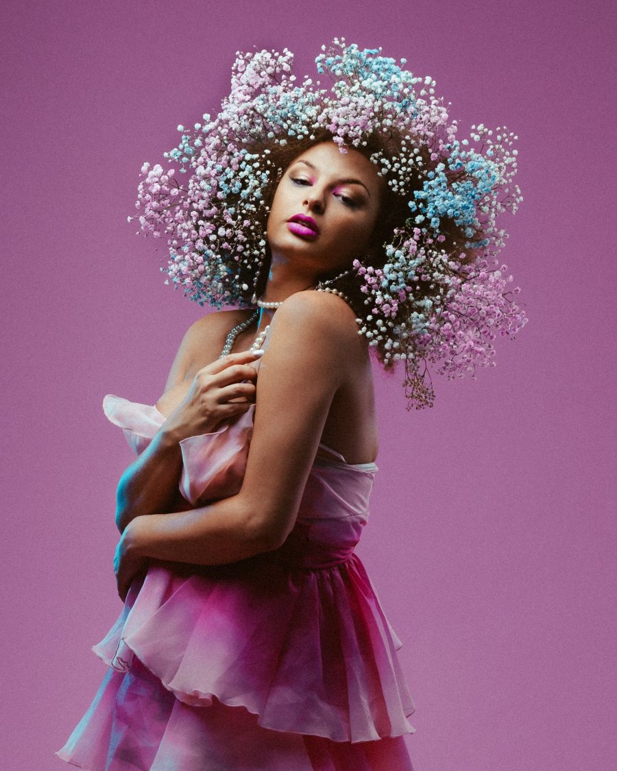 Miss Cairo, a queer performer, wearing and beautiful dress with blue and purple flowers in her hair.