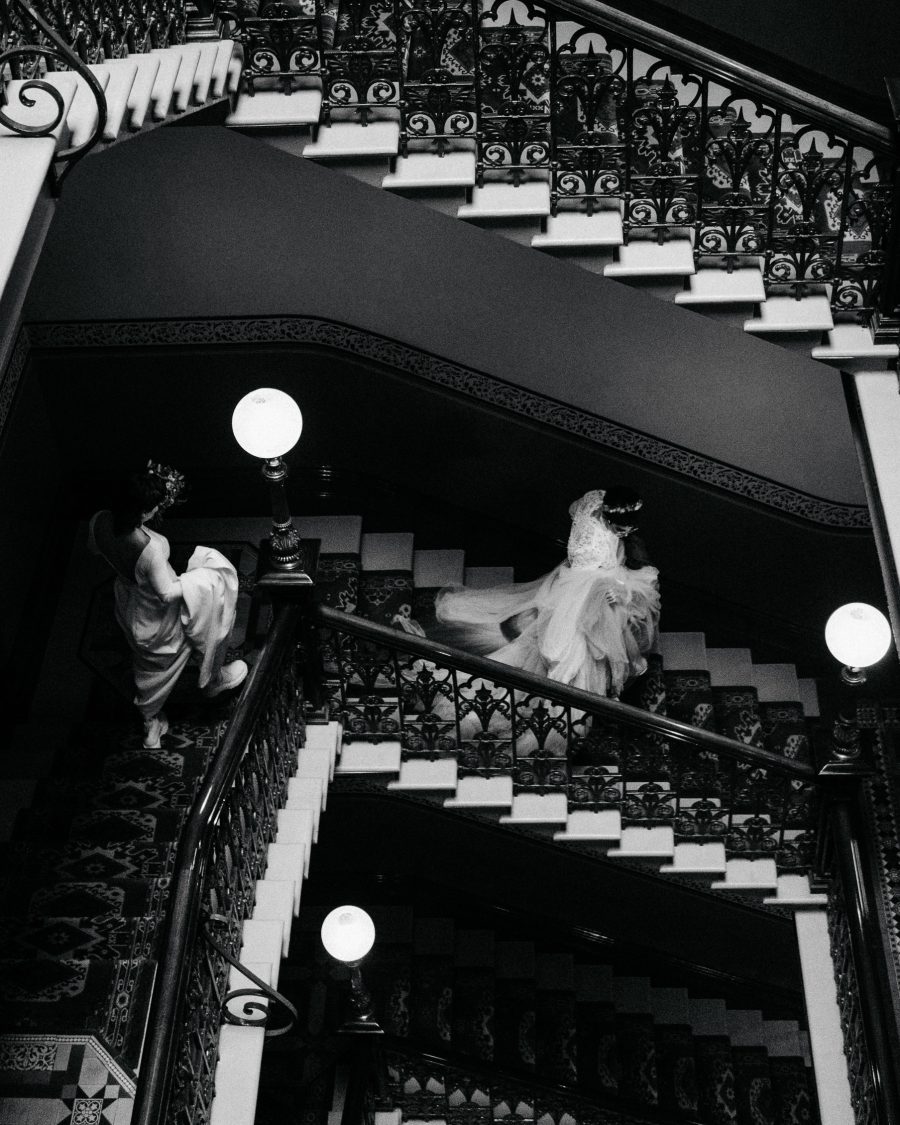 A couple walking down fancy stairs at their wedding, taken by Jacinta Oaten.