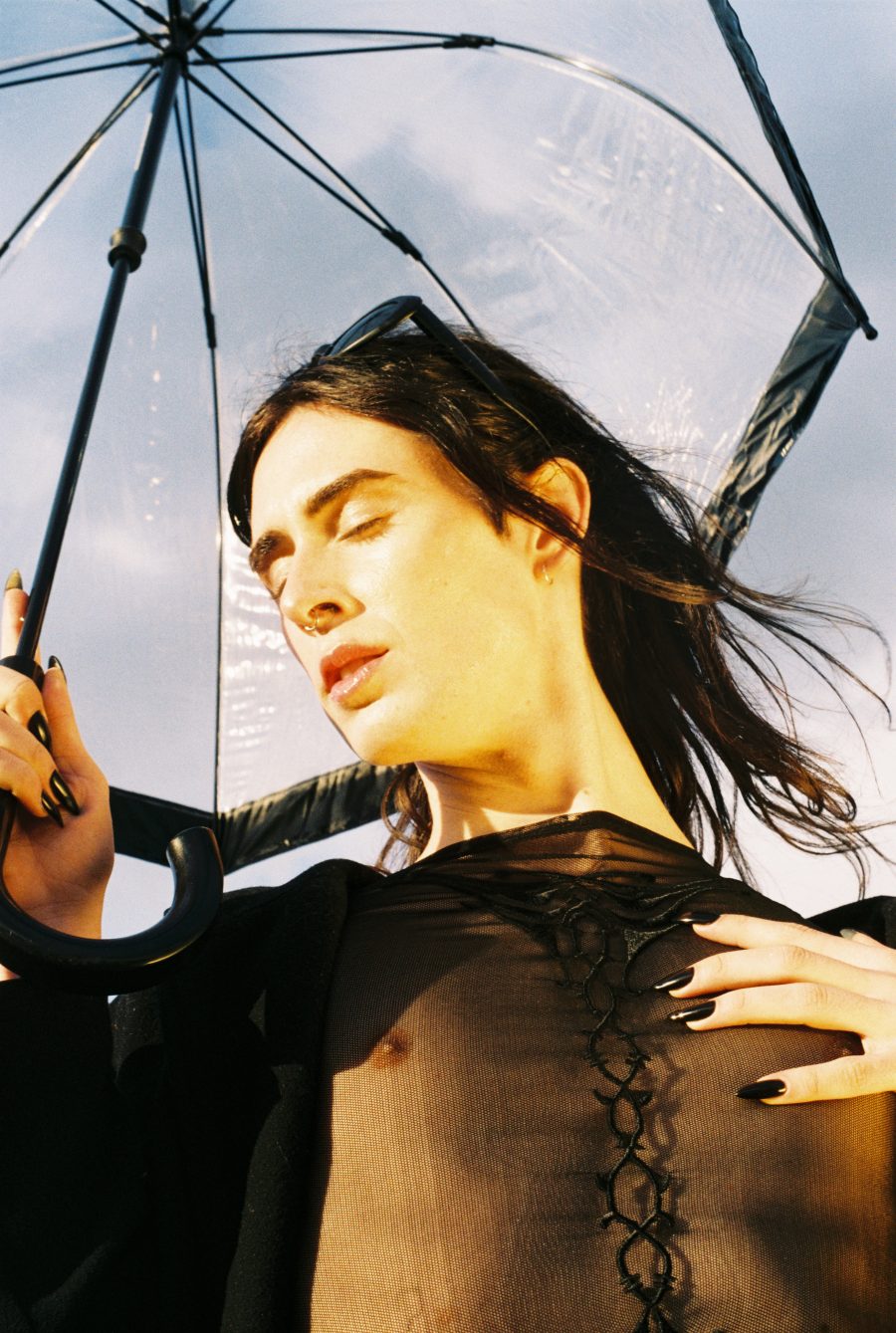 A person with closed eyes, holding an umbrella as their hair blows in the wind.