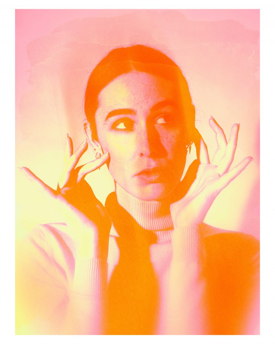 A person holding their face in orange, pink and yellow lighting.