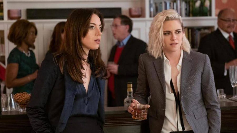 A still from Happiest Season of Aubrey Plaza and Kristen Stewart standing staring off-screen wearing suits. 